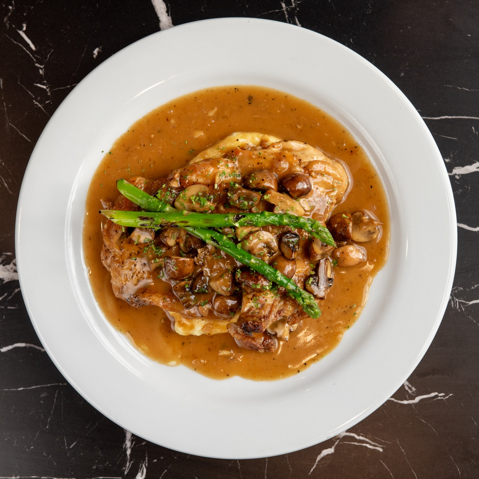 Lexie's Bistro's chicken dish with mushrooms, asparagus, and gravy on a white plate.