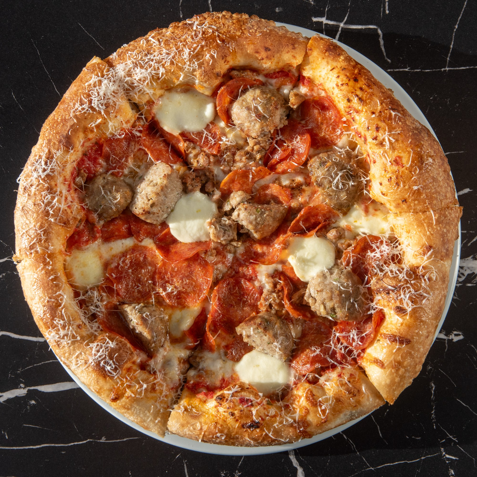 Lexie's Bistro's Italian pizza with pepperoni, sausage, and fresh mozzarella on a dark marble surface.