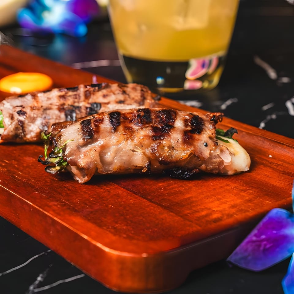 Grilled meat rolls with green filling and a yellow sauce on a wooden board at Lexie's Bistro.
