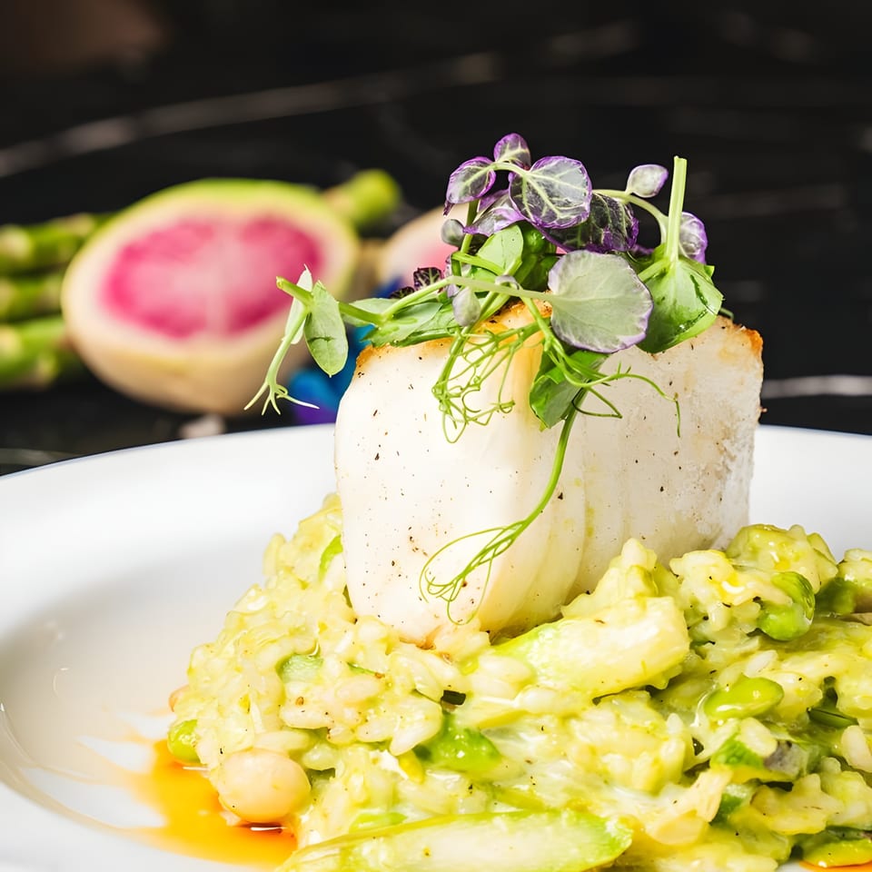 Seared fish fillet on a bed of green risotto, garnished with fresh herbs and microgreens.
