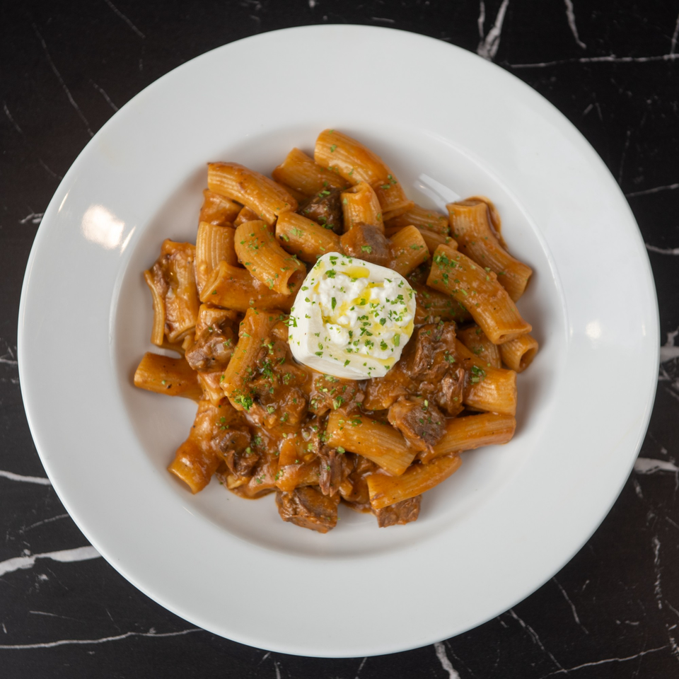 Rigatoni pasta with a rich meat sauce, topped with a dollop of fresh ricotta cheese and herbs.